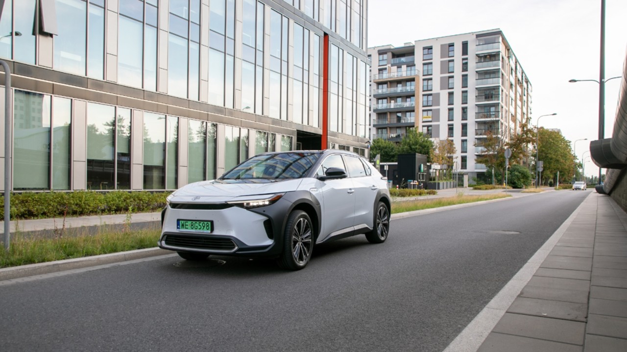 Zdjęcie Toyoty bZ4X poruszającej się po mieście na tle budynków mieszkalnych